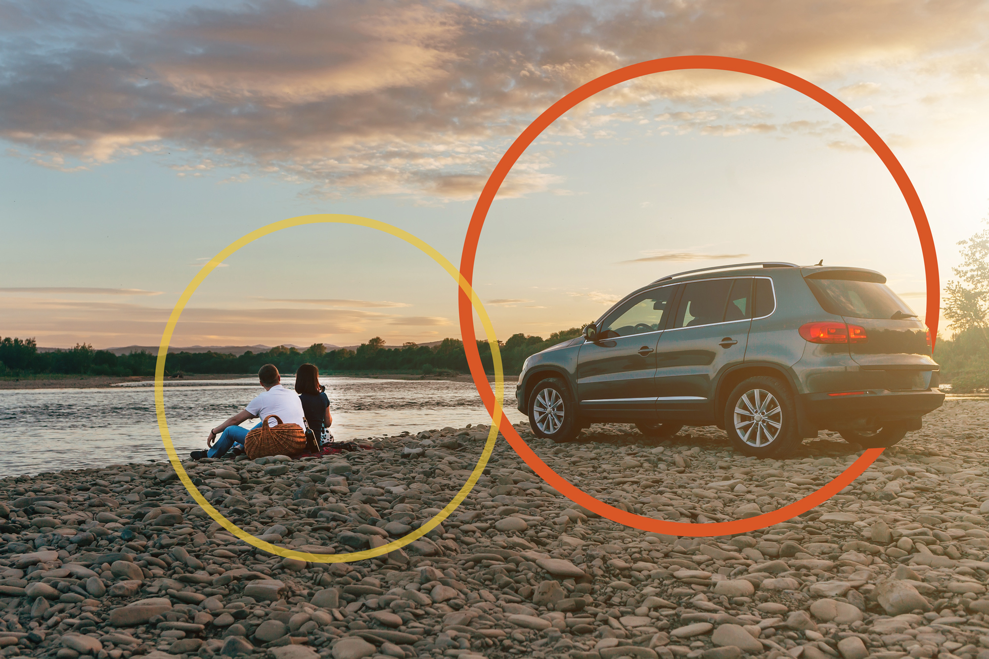 Couple sitting in sand on beach at sunset with SUV parked behind them