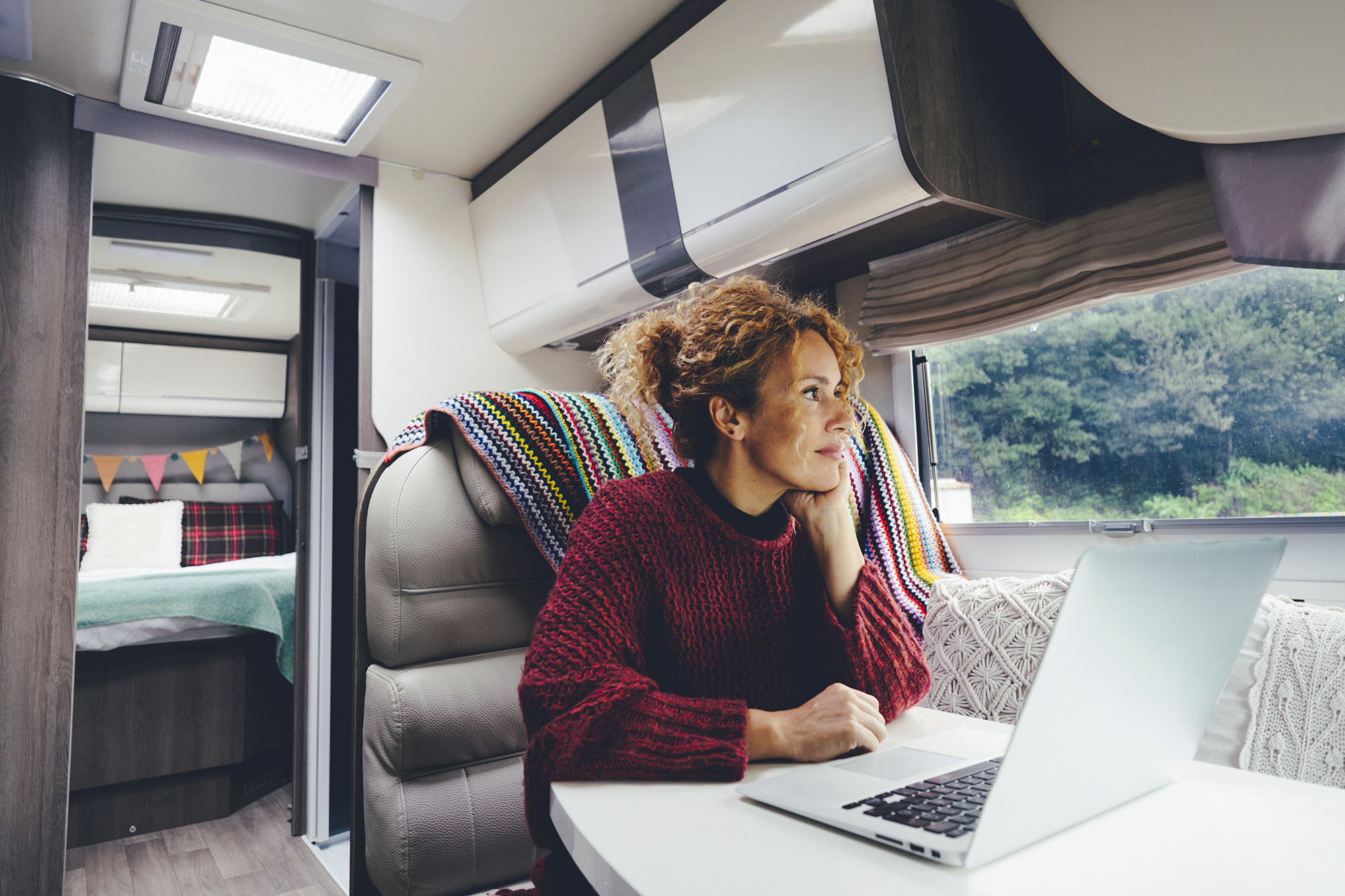 Woman sitting in RV remote working on laptop looking out window