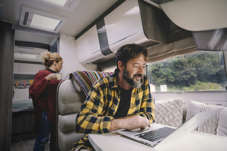Man working on laptop in camper RV with woman standing behind